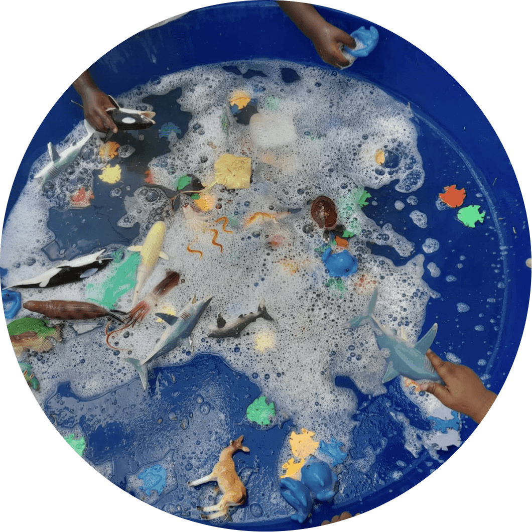 Children exploring a sensory play tray filled with water and toy sea animals